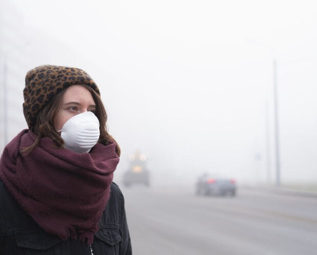 Kobieta w maseczce na tle zasmogowanego miasta